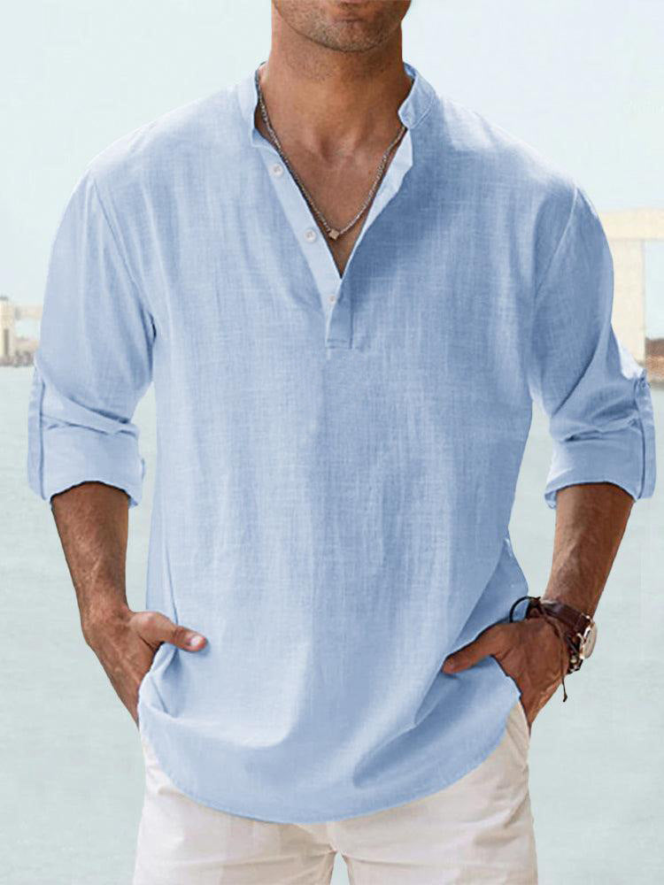 Man wearing a light blue shirt with rolled-up sleeves against a blurred outdoor background
