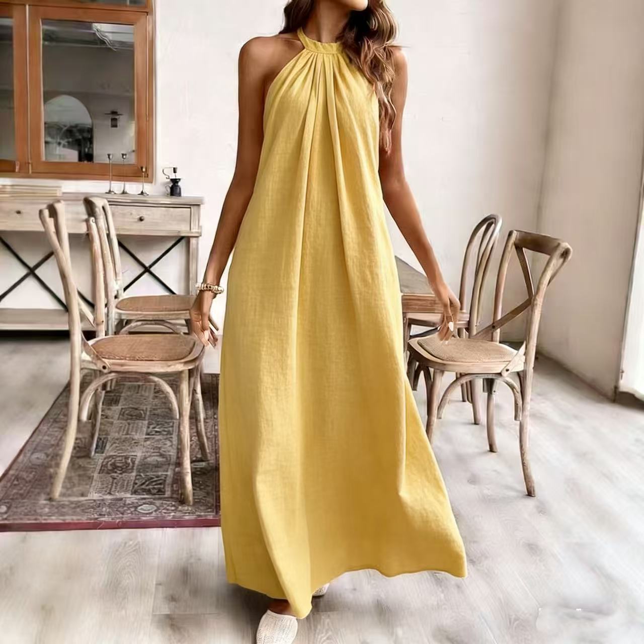 Woman in a yellow dress standing in a room with wooden chairs and a mirror.
