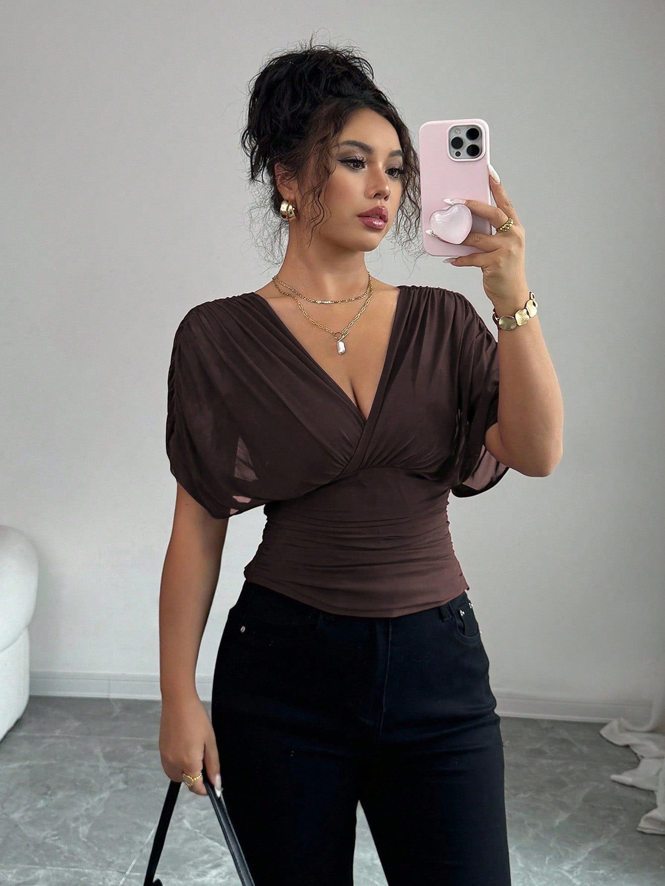 Woman taking a mirror selfie wearing a brown top and black pants in a room.