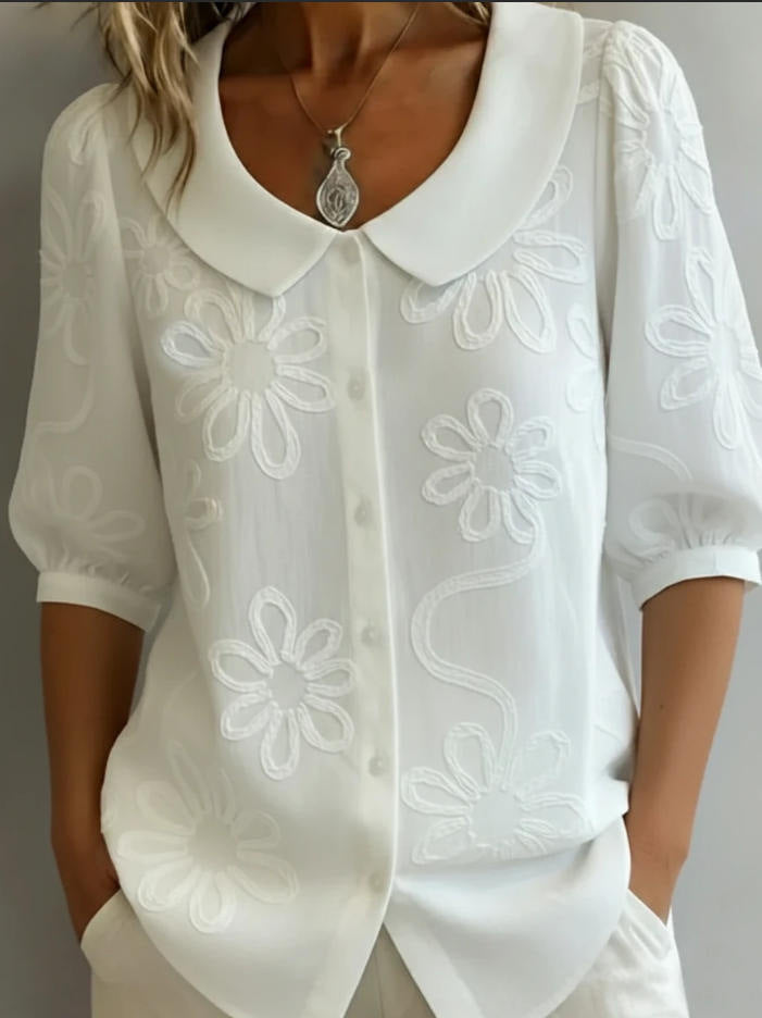 White blouse with floral embroidery on a plain background