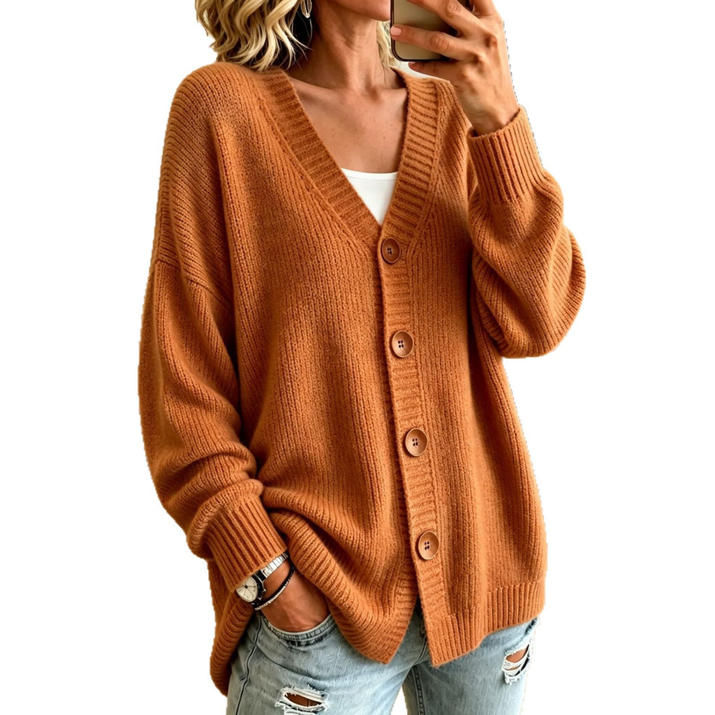 A woman wearing a rust-orange ribbed knit cardigan sweater with brown buttons, styled over a white top and light-wash distressed jeans, shown in a mirror selfie against a white background.