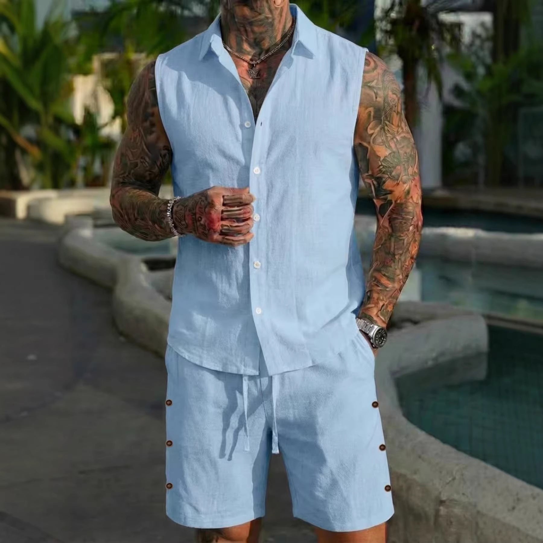Man wearing a light blue sleeveless shirt and shorts set with tattoos, standing by a pool.