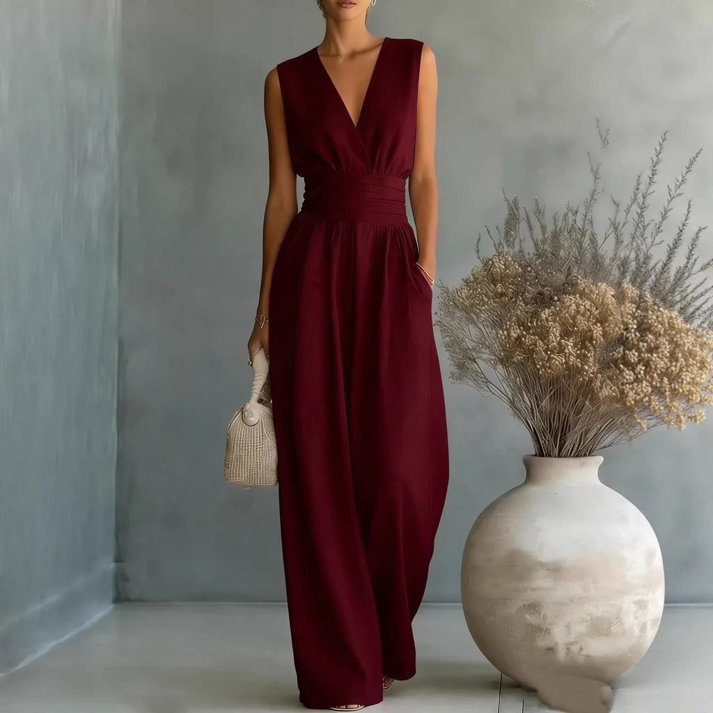 Woman in a burgundy dress standing next to a vase with dried flowers against a gray wall.