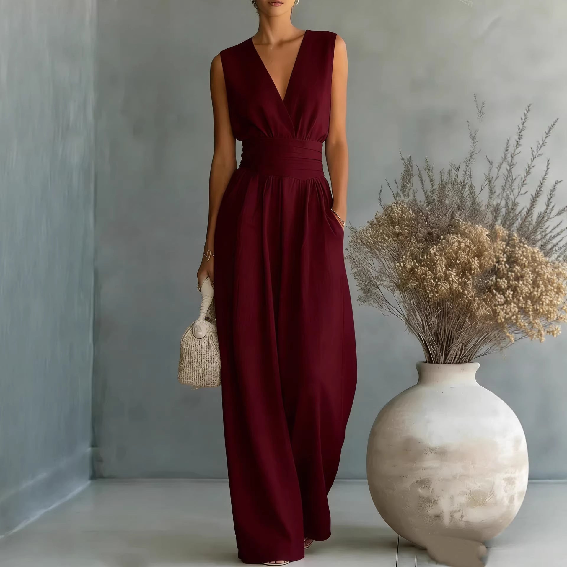 Woman in a burgundy dress standing next to a vase with dried flowers against a gray wall.