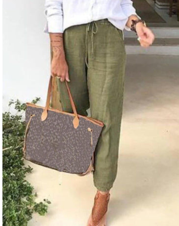 Person holding a patterned tote bag wearing green pants and brown shoes.