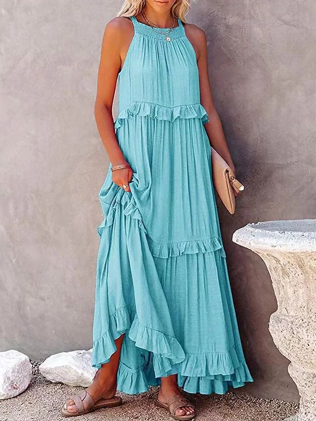 Woman wearing a turquoise dress with ruffled layers against a stone wall.