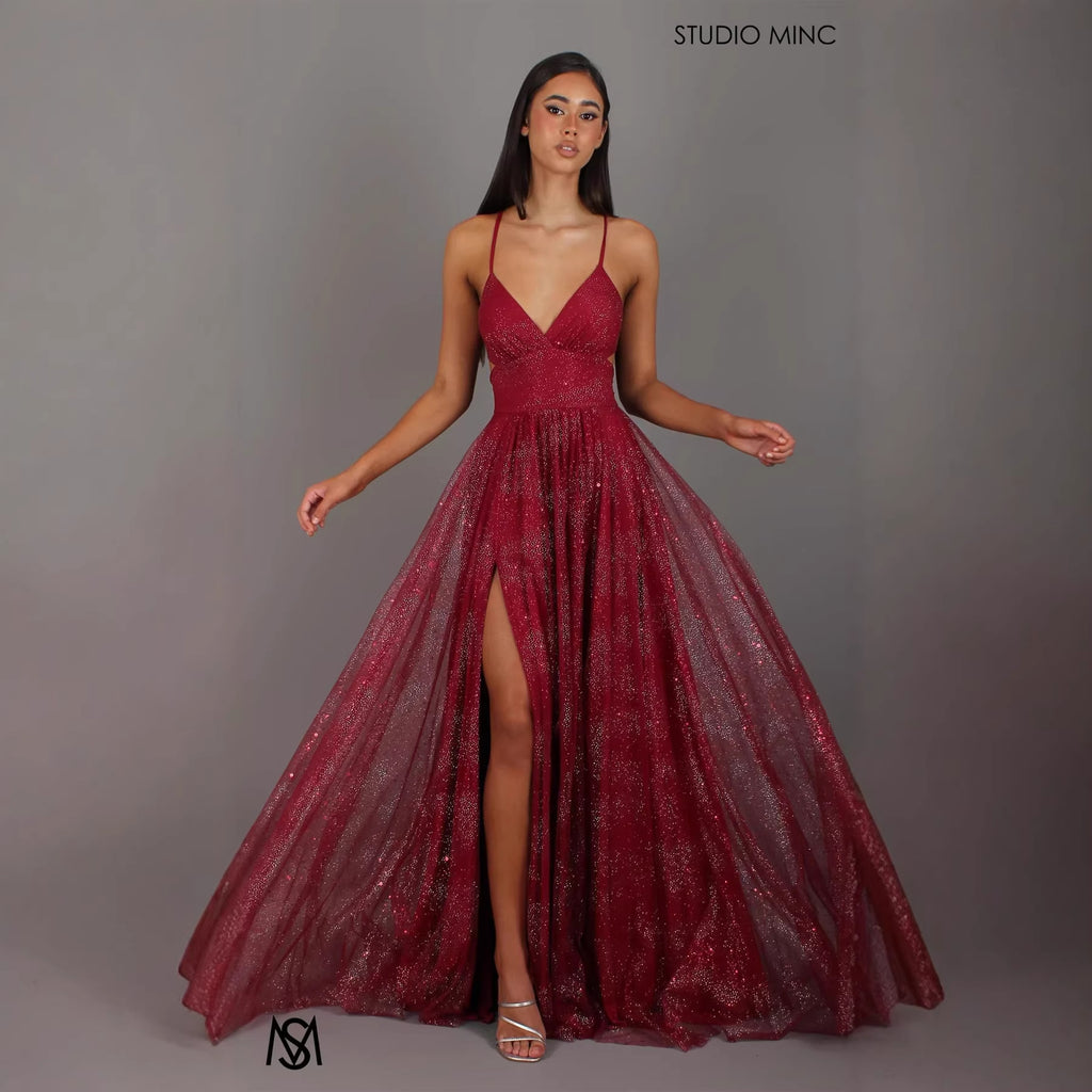 Model wearing a red evening gown with a slit on a gray background, branded 'Studio Minc'.