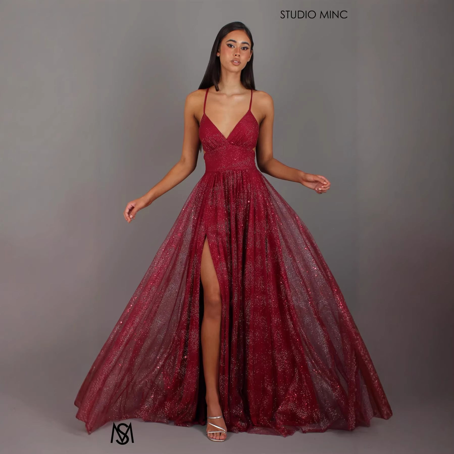 Model wearing a red evening gown with a slit on a gray background, branded 'Studio Minc'.