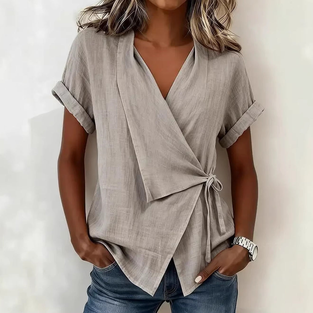 Woman wearing a light gray wrap top with short sleeves against a white background