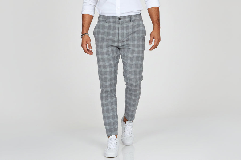 Person wearing gray plaid pants and white sneakers on a plain background