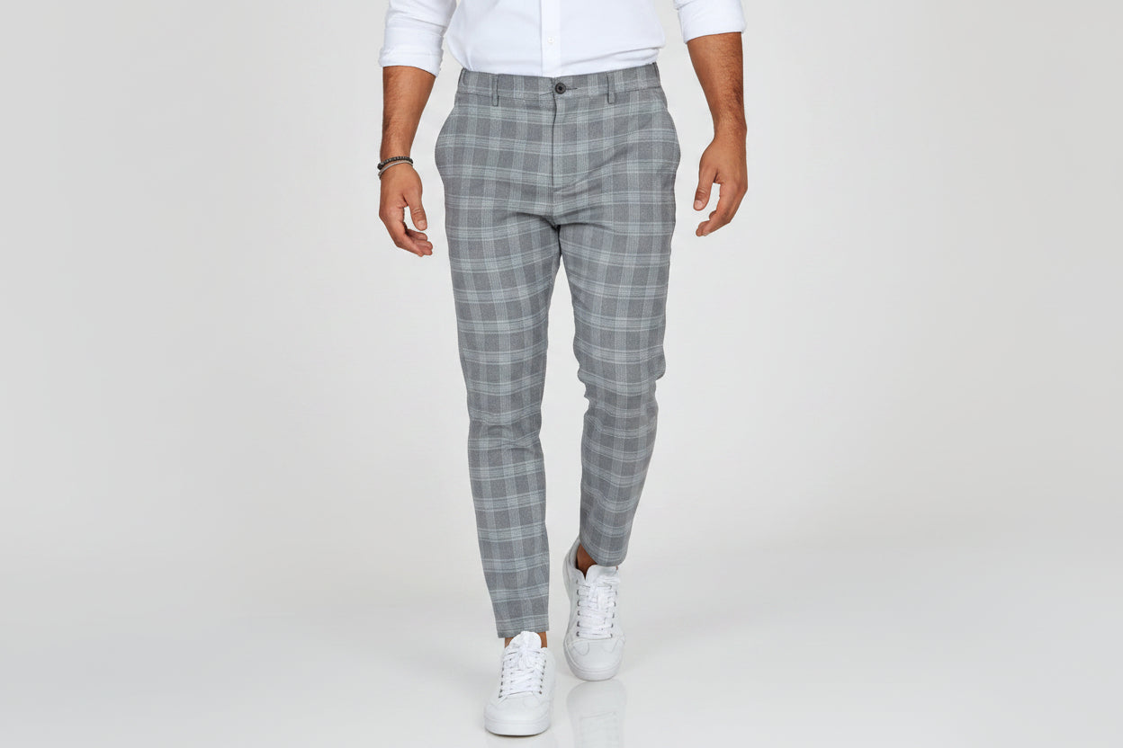 Person wearing gray plaid pants and white sneakers on a plain background