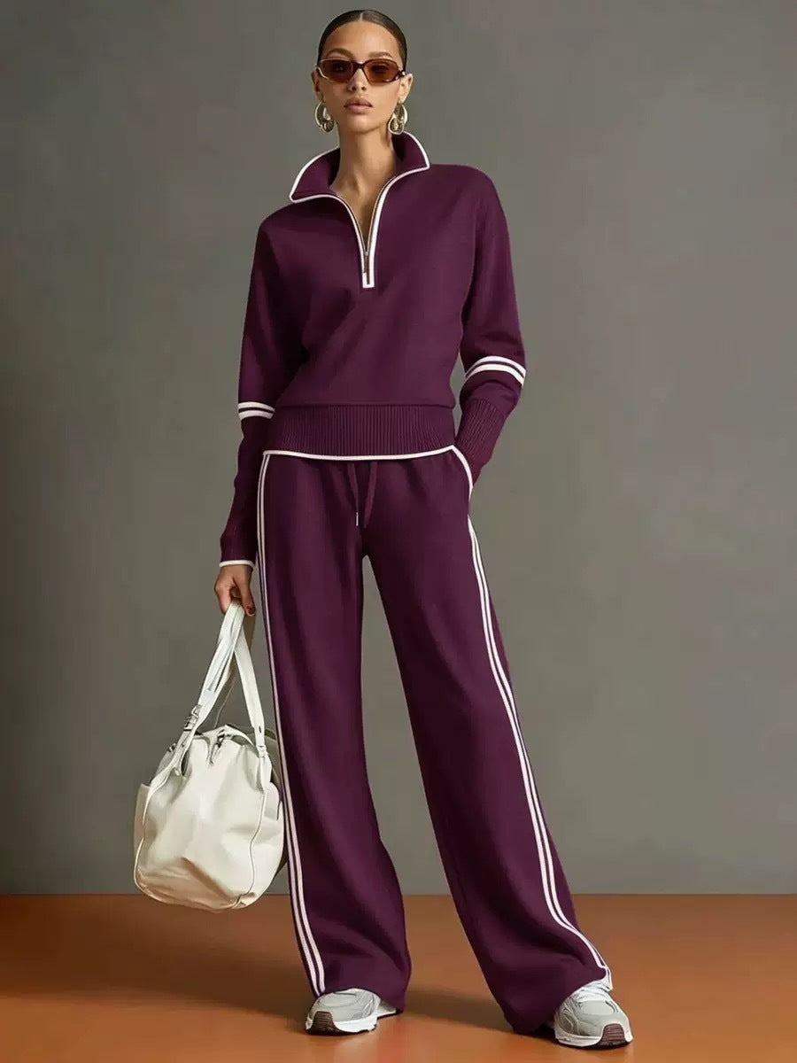 Person wearing a purple tracksuit with white stripes, holding a white bag against a gray background.