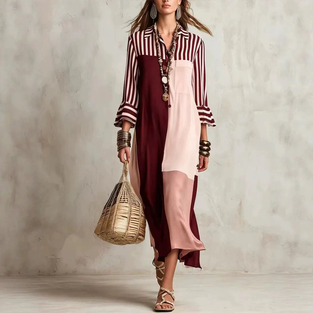 Woman wearing a striped shirt over a long dress with a woven bag against a plain background