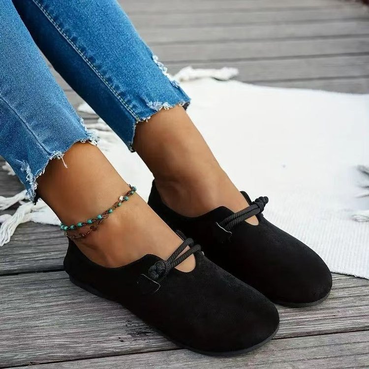 Black loafers worn with blue jeans on a wooden floor.