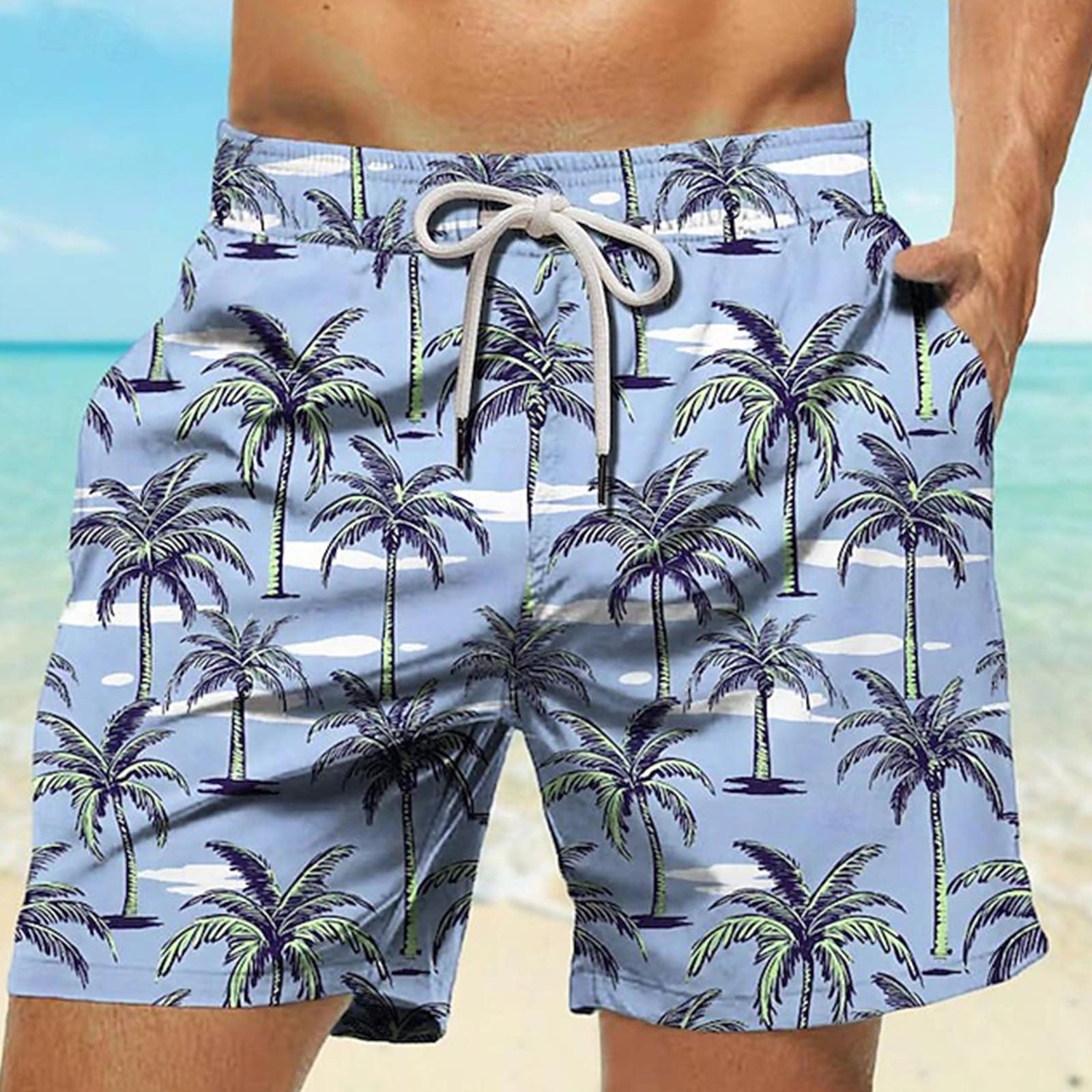 Blue swim shorts with palm tree pattern worn by a person on a beach.