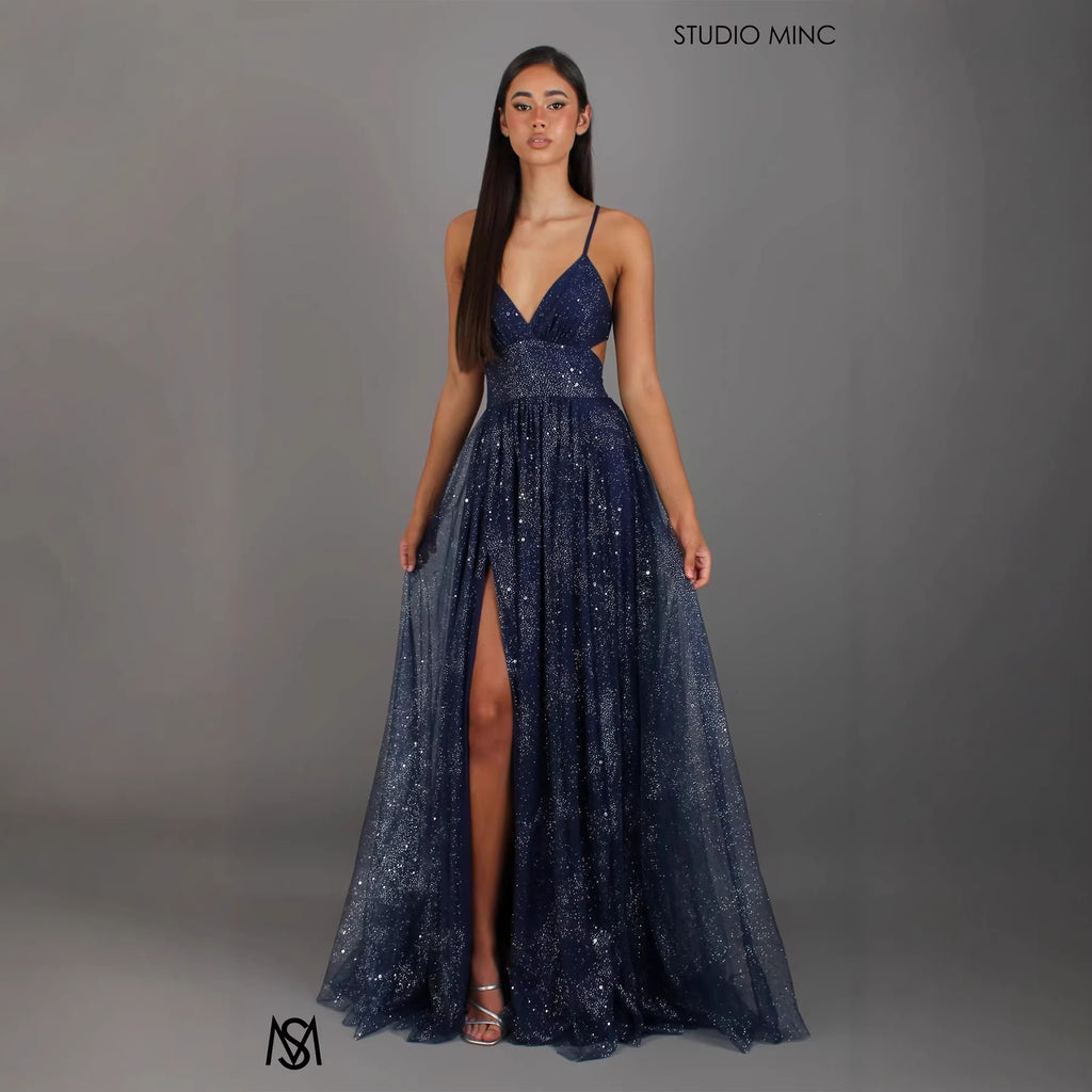 Navy blue evening gown with a high slit on a gray background, brand 'Studio MinC' visible.