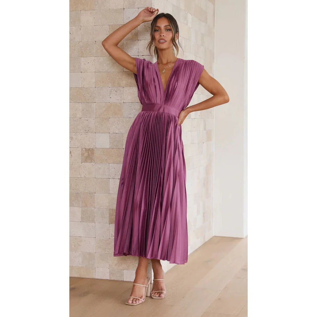 Woman wearing a purple pleated dress against a beige wall.