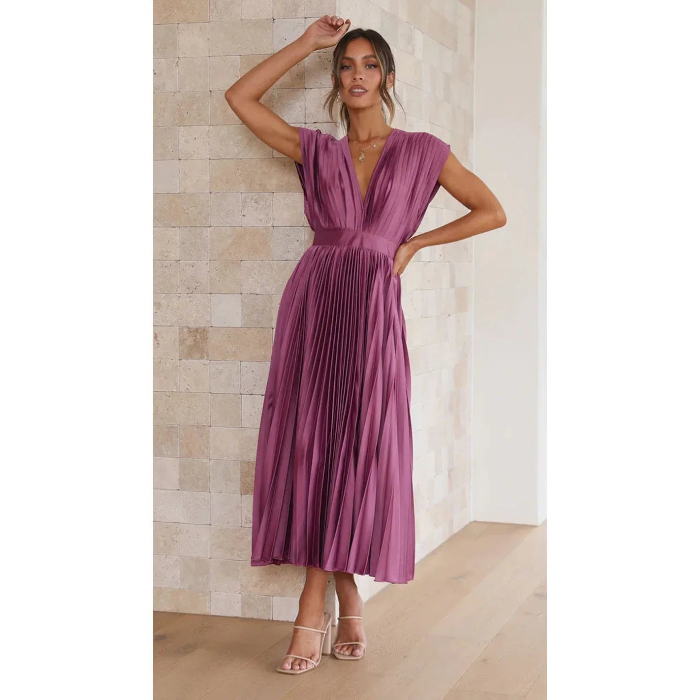 Woman wearing a purple pleated dress against a beige wall.