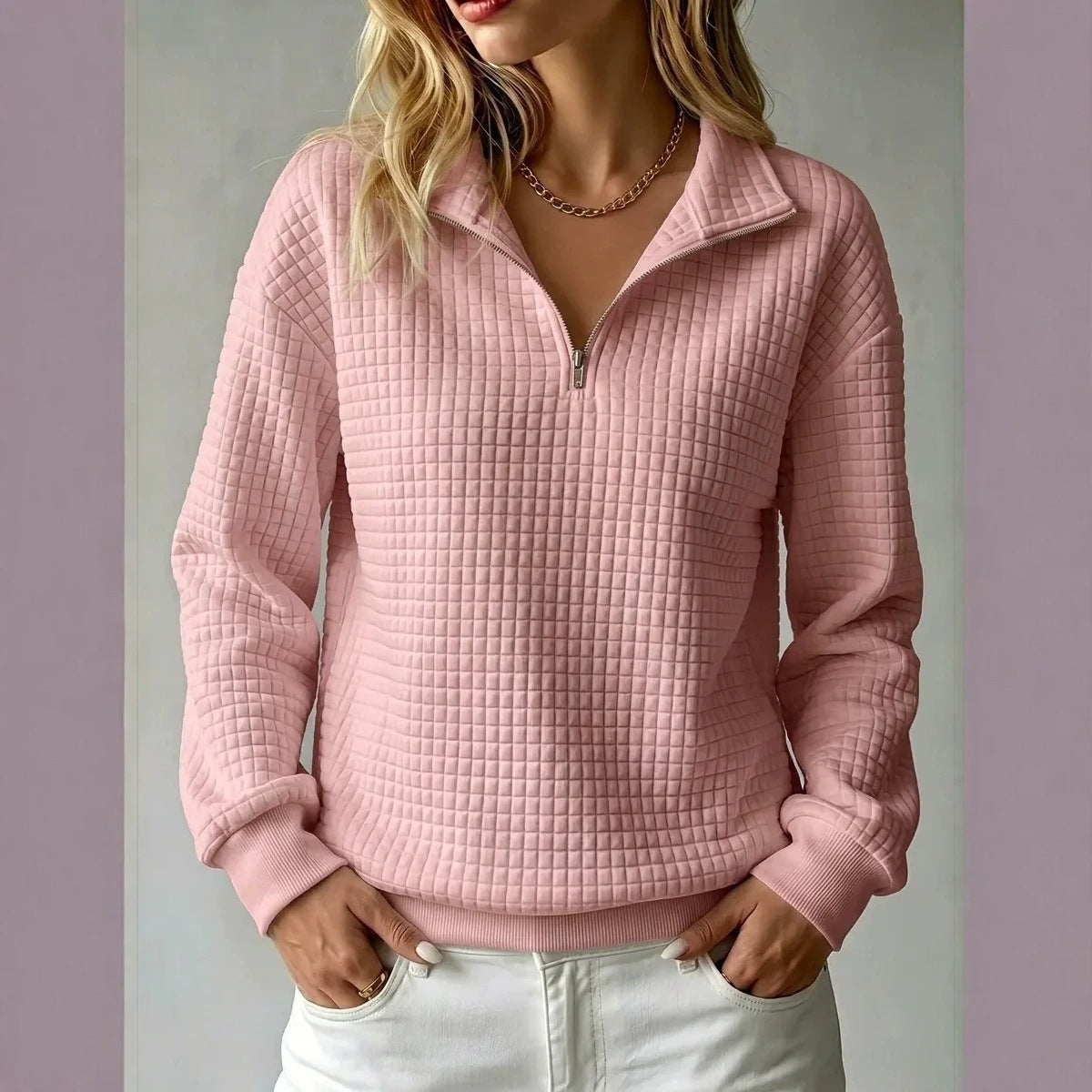 A woman wearing a pink waffle-textured quarter-zip pullover sweater with a stand collar, paired with white pants, shown against a neutral studio background.