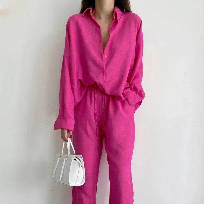 Woman in bright pink ZA-Zola blouse and pants holding white handbag against neutral wall