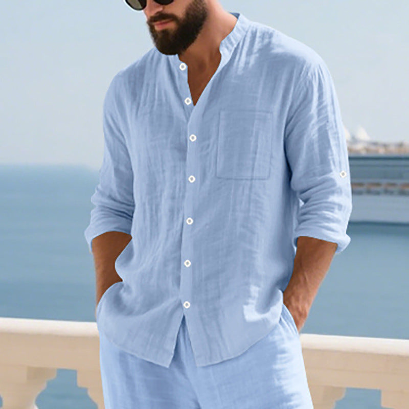 Man wearing a light blue linen shirt and pants by the sea.