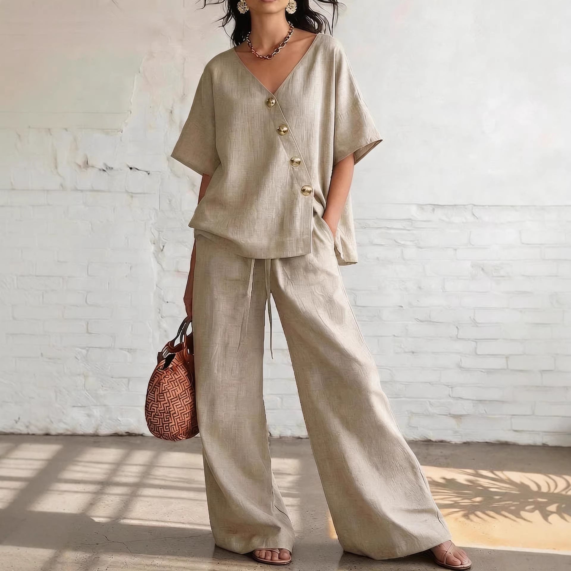 Woman wearing a beige outfit with wide-leg pants against a white brick wall.