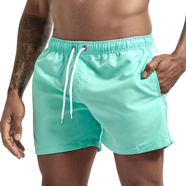 Turquoise swim shorts with a white drawstring on a person against a neutral background