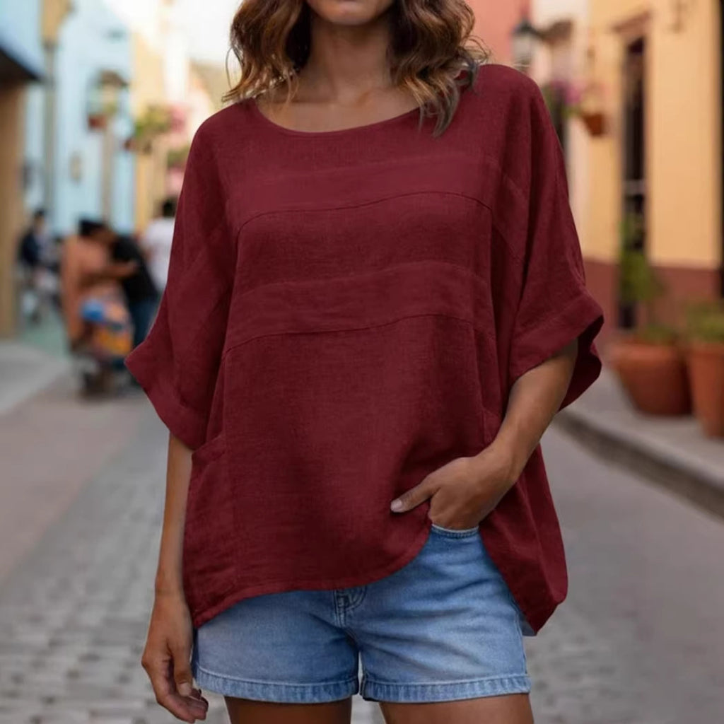 Person wearing a burgundy oversized top and denim shorts on a street.