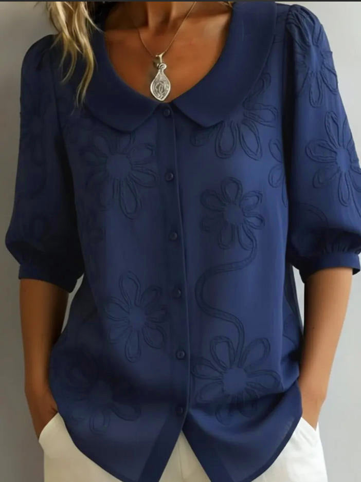 Navy blue blouse with floral patterns worn by a person against a neutral background
