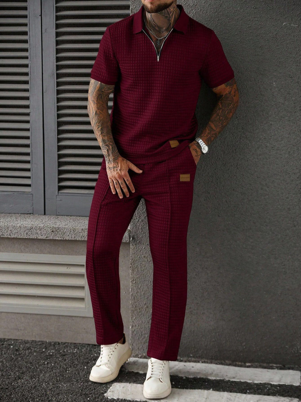 Man wearing a maroon outfit with white sneakers against a gray wall.