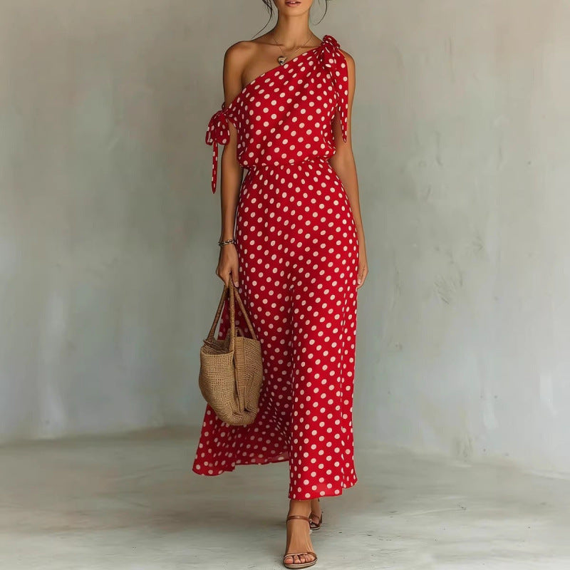 Woman wearing a red polka dot dress holding a woven bag against a plain background