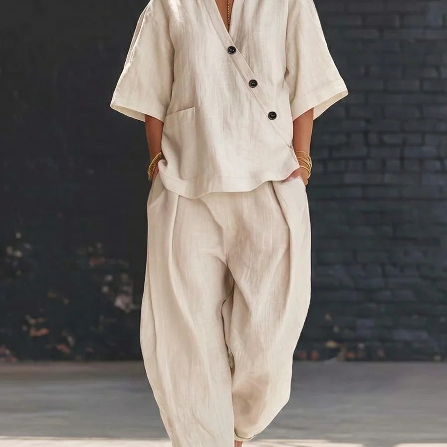 Person wearing a beige outfit with black buttons against a dark brick wall.
