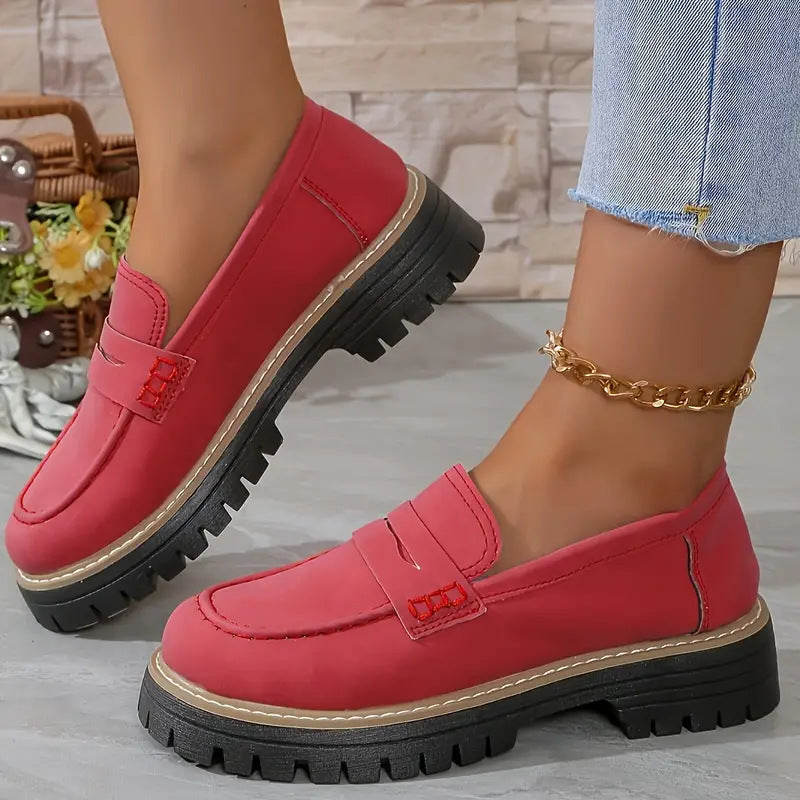 Red loafers with black soles worn by a person, with a blurred background.