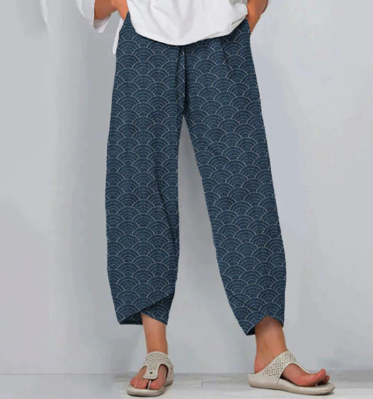 Person wearing blue patterned pants and white sandals on a plain background