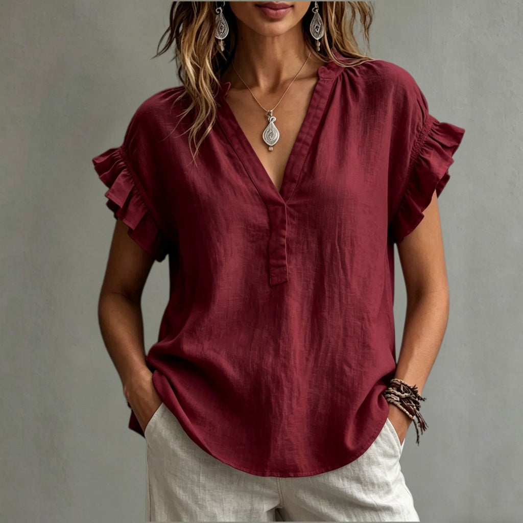 Woman wearing a burgundy blouse with ruffled sleeves against a neutral background
