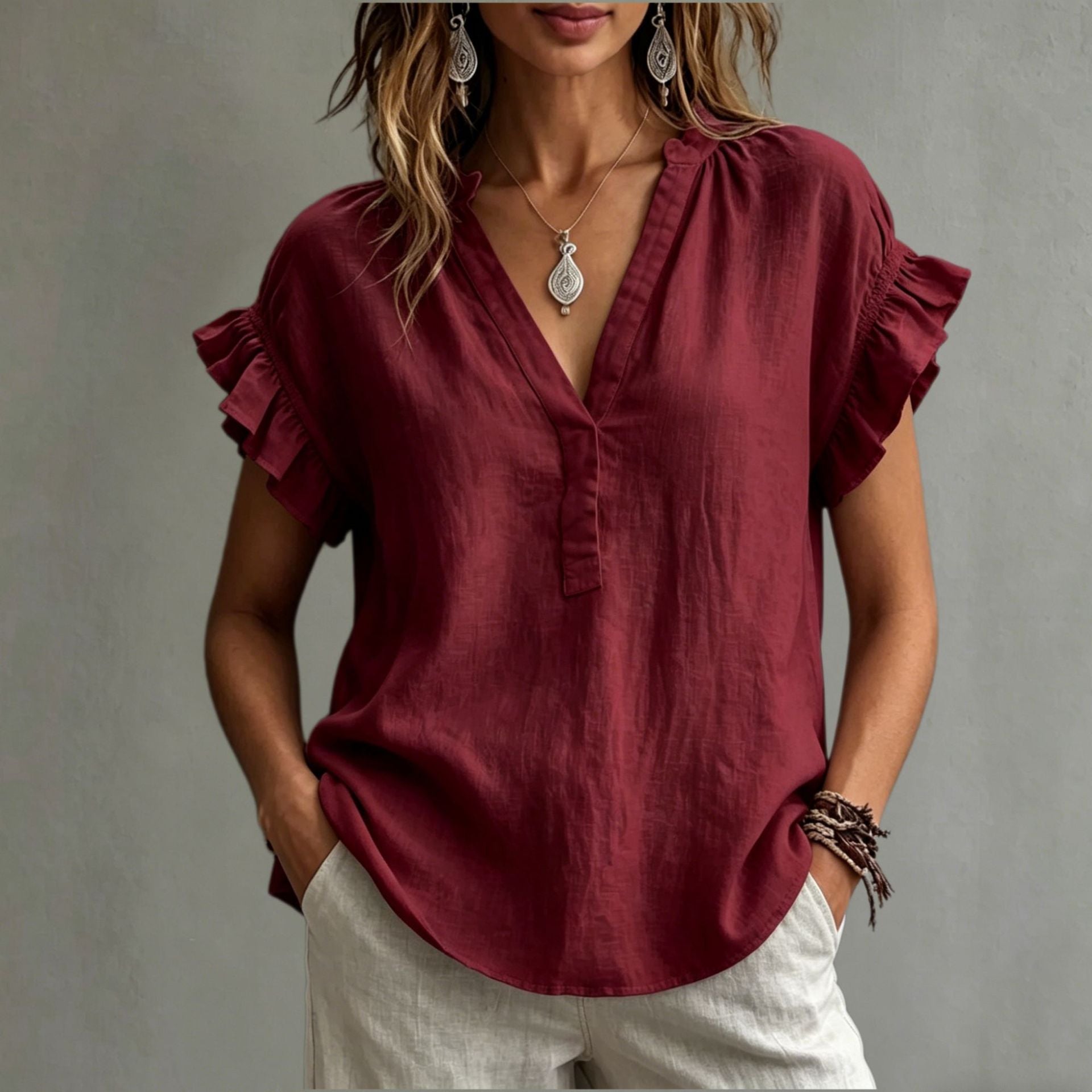 Woman wearing a burgundy blouse with ruffled sleeves against a neutral background