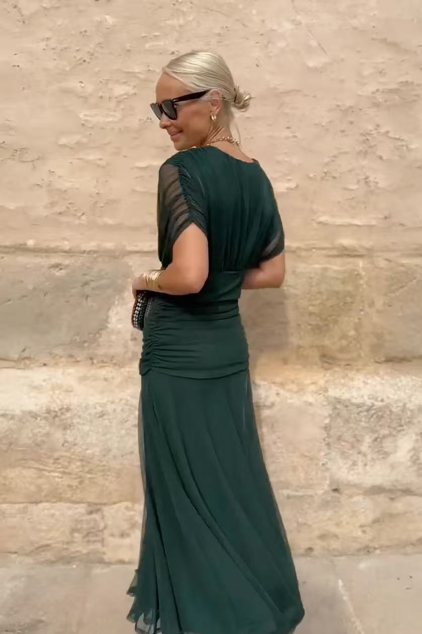 Woman in a green dress standing against a stone wall.