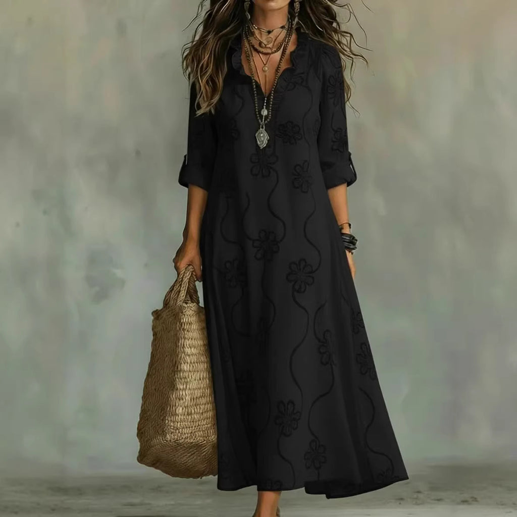 Woman wearing a black dress with floral patterns, holding a woven bag against a neutral background