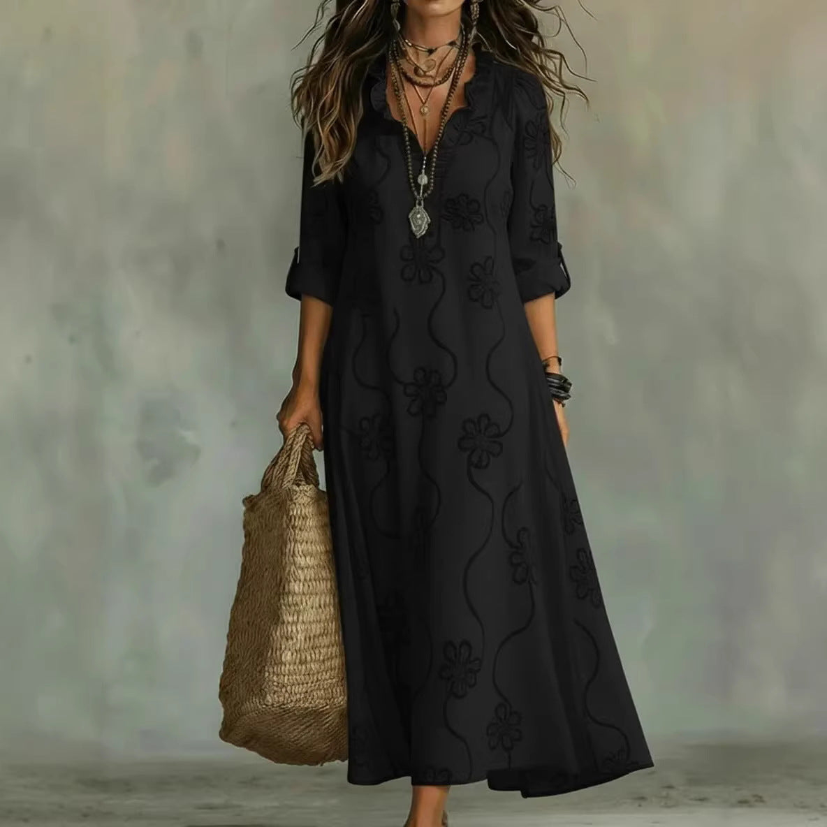 Woman wearing a black dress with floral patterns, holding a woven bag against a neutral background