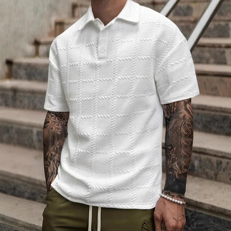 Person wearing a white textured polo shirt and green pants with tattoos on arms, standing on steps.