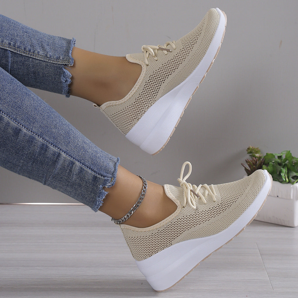 Beige sneakers with white soles worn with blue jeans on a neutral background