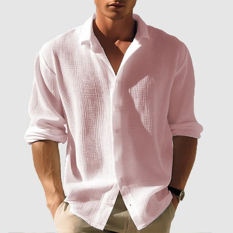 Man wearing a light pink button-up shirt with rolled-up sleeves on a plain background