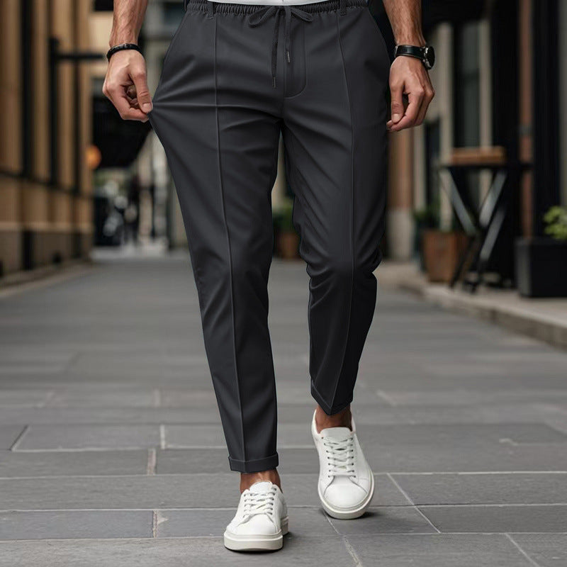 Person wearing dark gray pants and white sneakers on a city street.