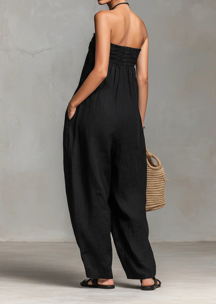 Person wearing a black jumpsuit holding a woven bag against a gray background