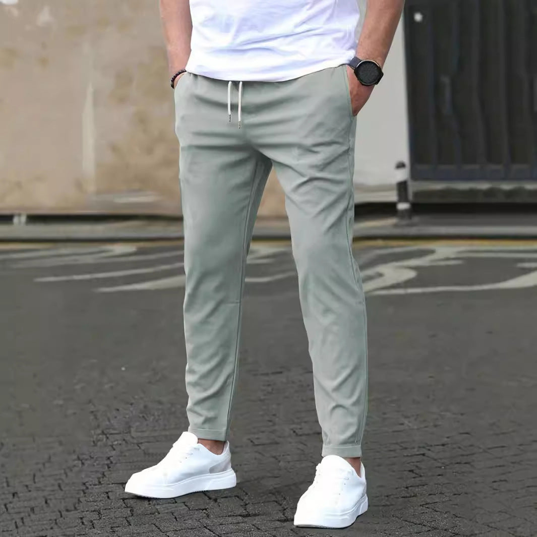 Person wearing light gray jogger pants and white sneakers on a street.