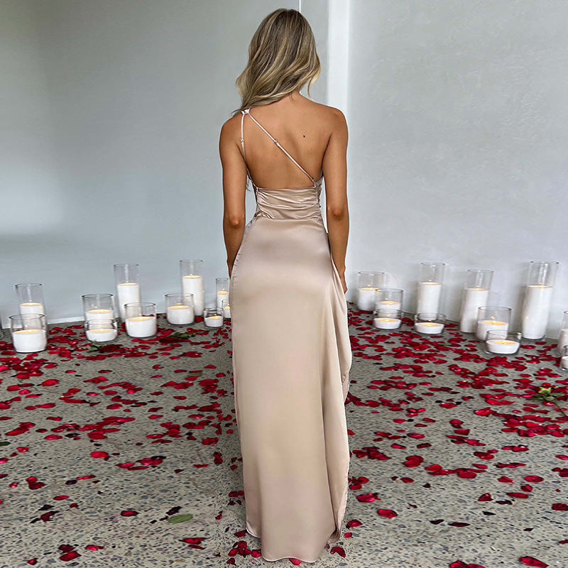 Woman in a beige evening gown standing in a room with candles and red rose petals on the floor.