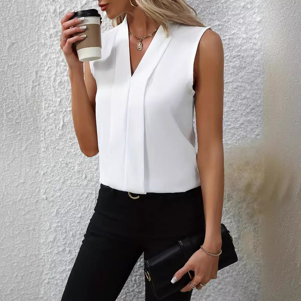 Woman wearing a white sleeveless top and black pants, holding a coffee cup against a light gray background.