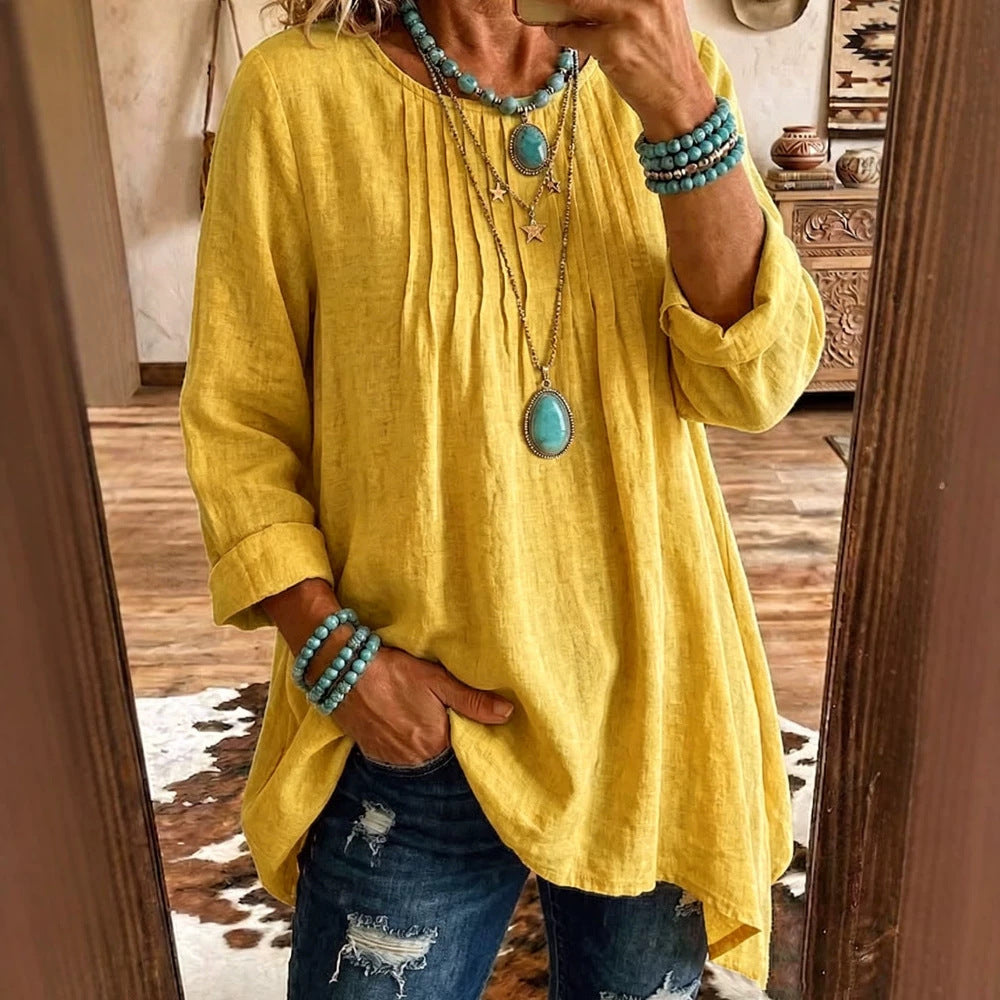A woman takes a mirror selfie wearing a loose, yellow linen-blend tunic top with three-quarter sleeves, paired with distressed blue jeans and layered turquoise jewelry.
