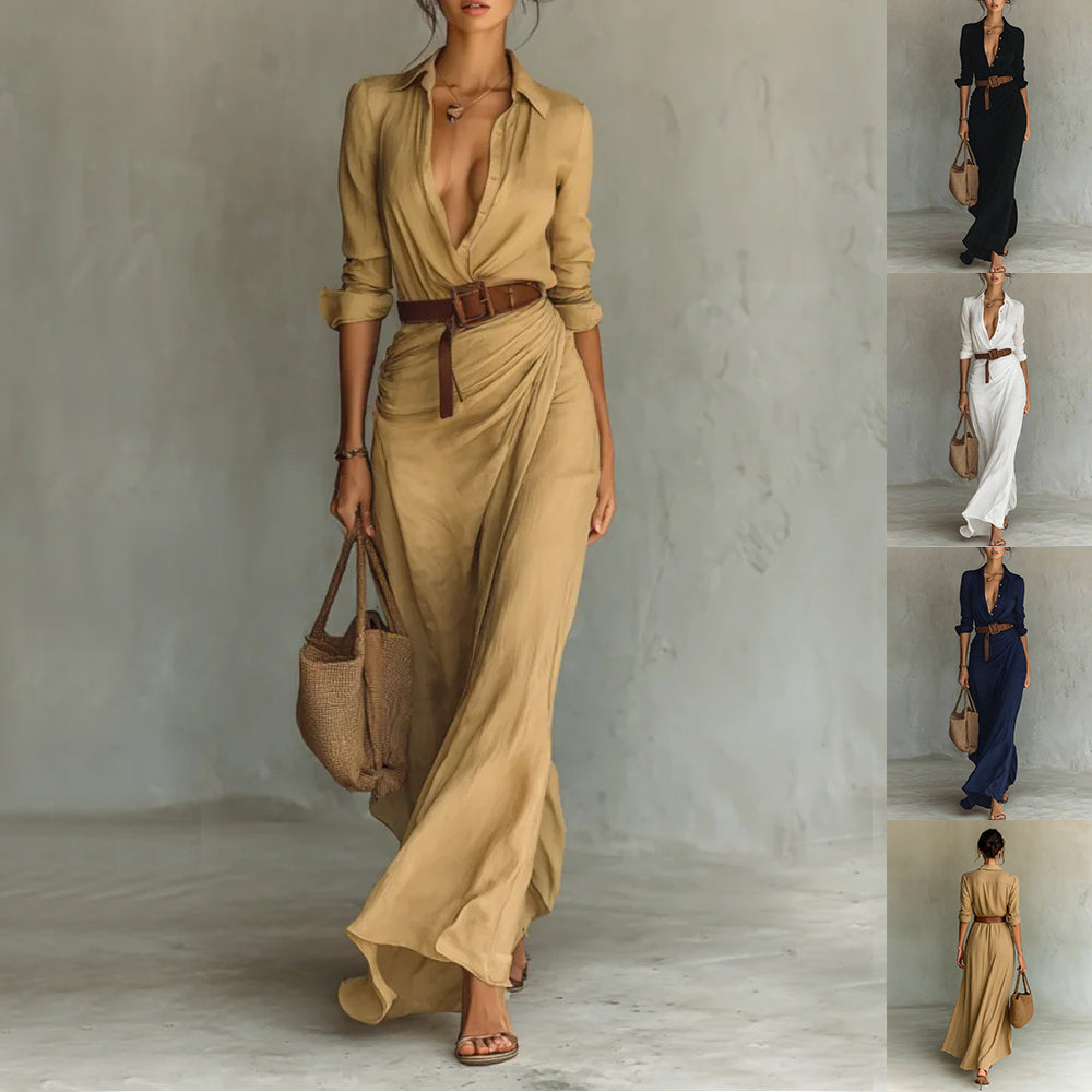 Woman in a long beige dress with a belt holding a bag against a neutral background.