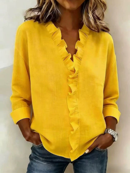 Person wearing a yellow blouse with ruffled details and blue jeans against a neutral background